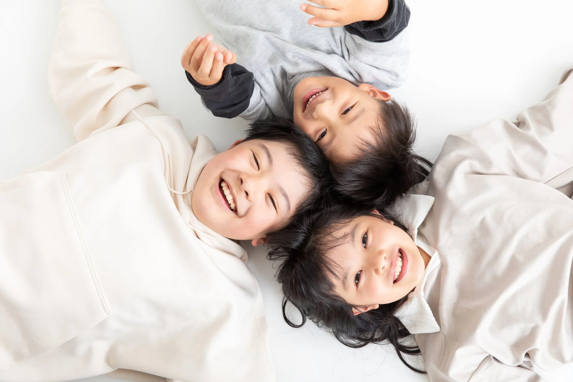 床に寝転んで笑顔を見せる3人の子どもたち